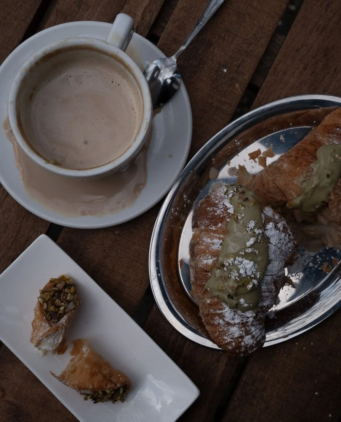 Cappuccino neben einem Cornetto mit Pistaziencreme und kleinem Gebäck