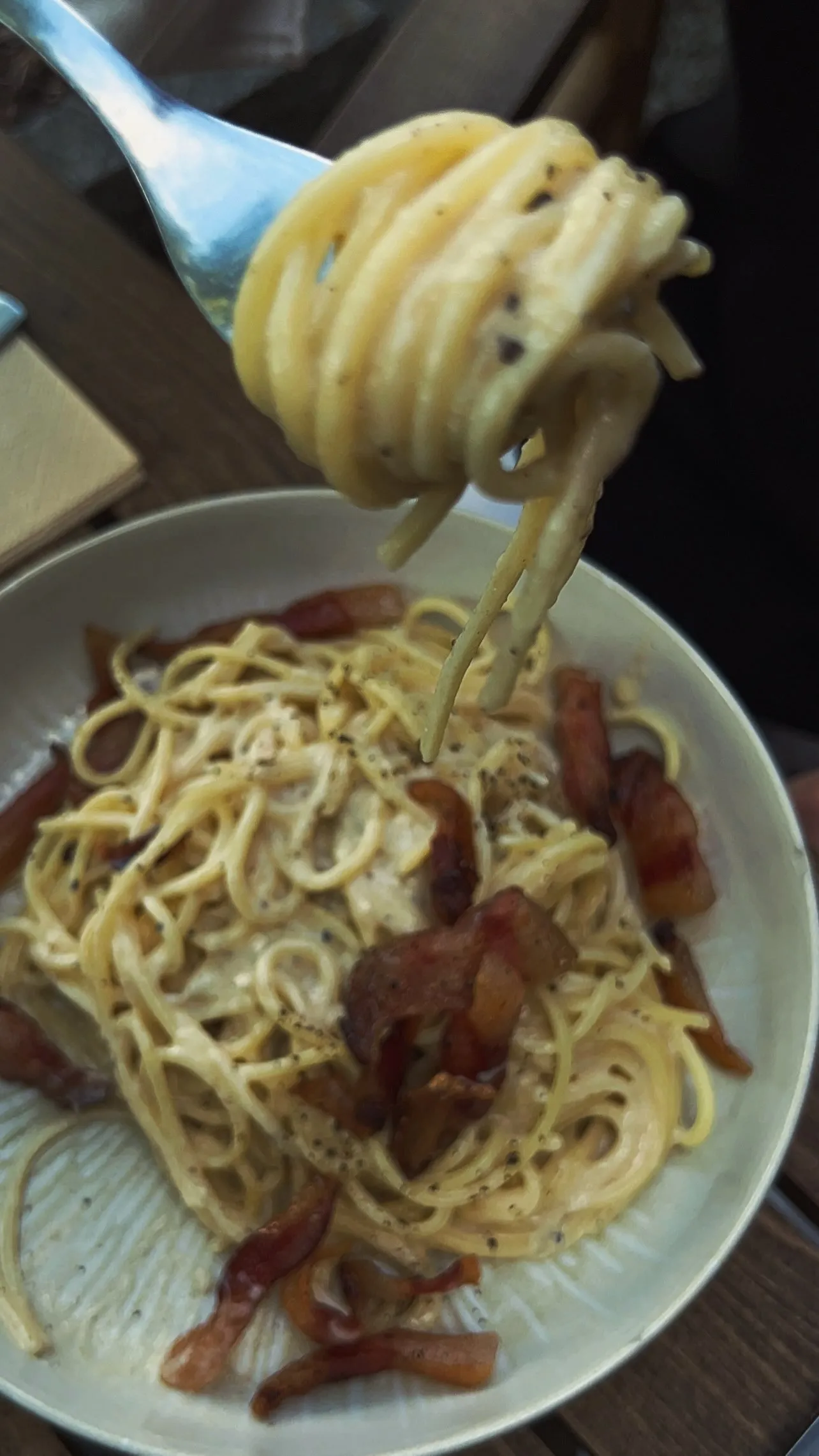Spaghetti Carbonara mit knusprigem Guanciale, eine Gabel hebt eine Portion an