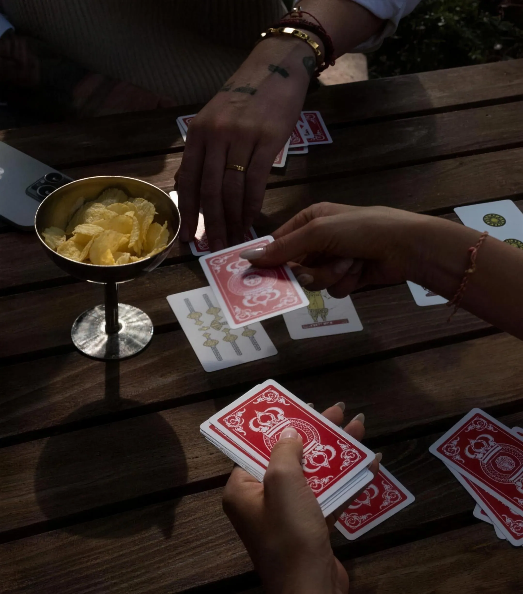 Zwei Hände beim Kartenspiel an einem Holztisch, daneben eine Schale mit Chips