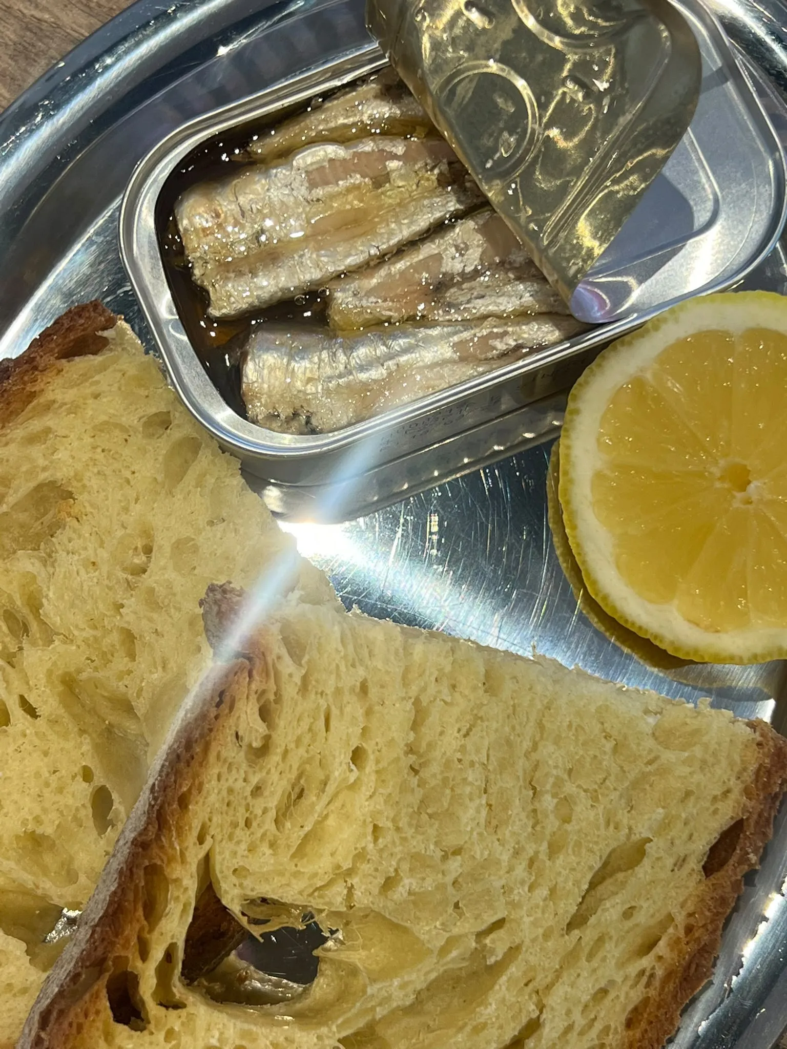 Geöffnete Dose Sardinen mit Brot und Zitrone auf einem Silbertablett